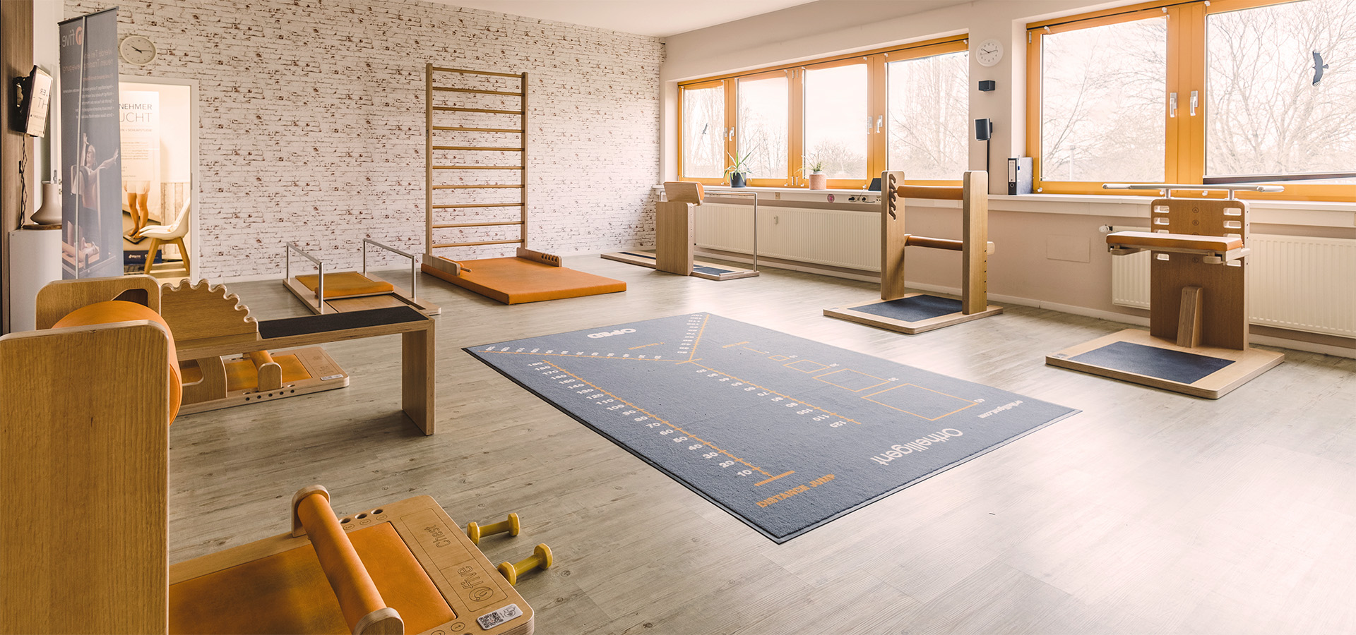 Heller, geräumiger Physiotherapie-Raum mit Holz-Physioausrüstung (z. B. Leiter, Messmatte) und modernem Design, ideal für Schmerzreduktion, Beweglichkeitstraining und gesundheitliche Prävention.