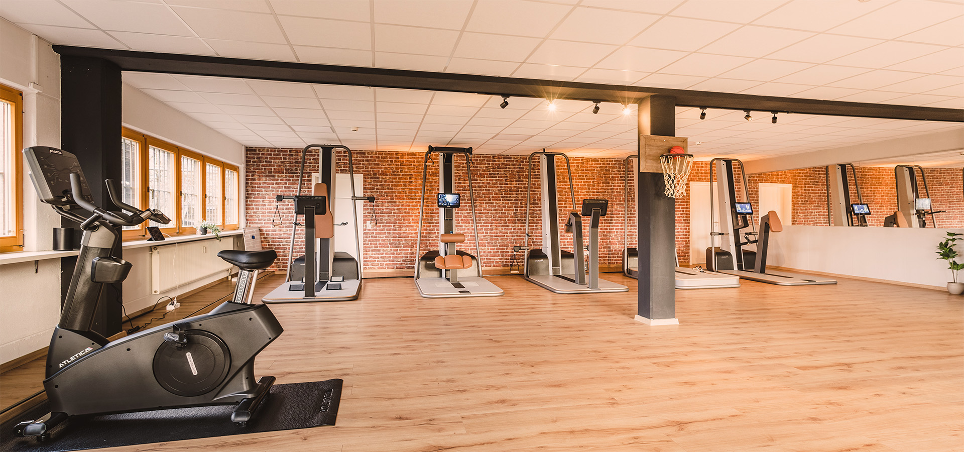 Modernes Gesundheitsstudio der Physio Five Physiotherapiepraxis in Merenberg mit hochwertigen Trainingsgeräten, Backsteinwand, hellem Holzboden und Basketballkorb – hier wird klassische Physiotherapie mit medizinischem Gesundheitstraining verbunden.