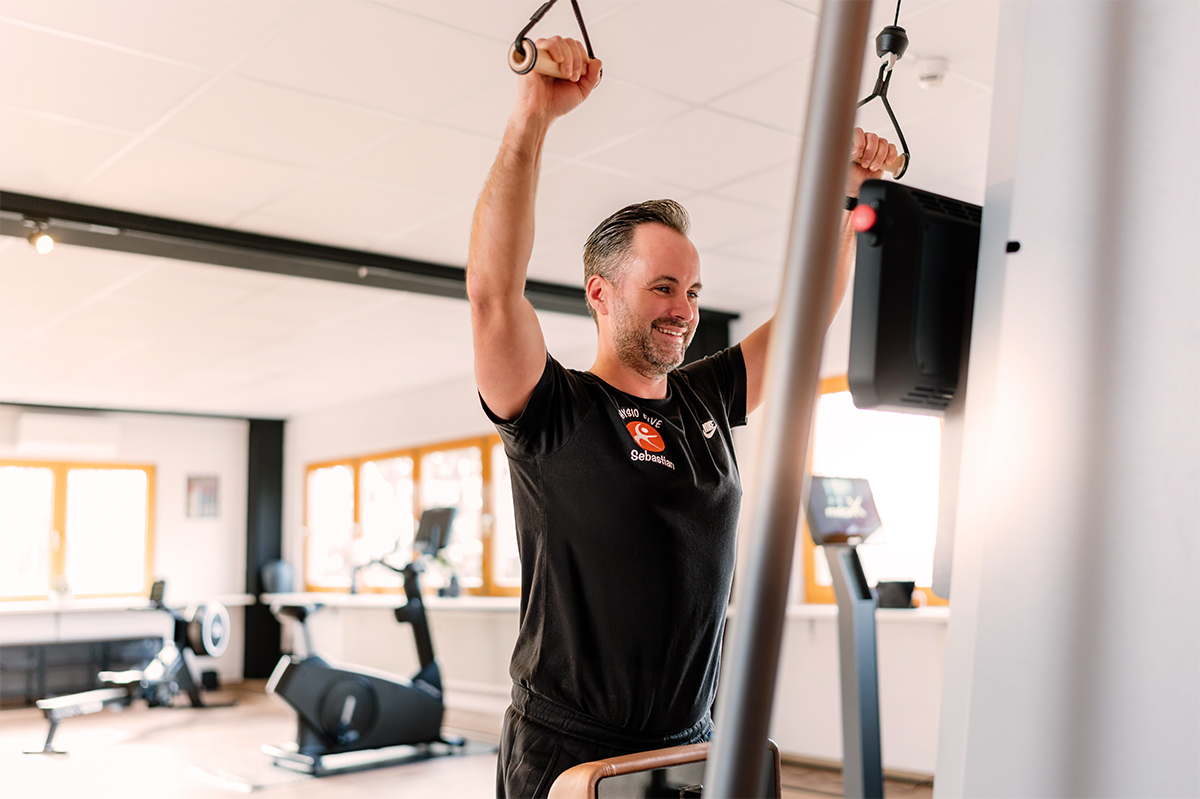 Ein Mann trainiert mit einem Kabelzug in einem modernen Gesundheitsstudio der Physio Five Physiotherapiepraxis, die klassische Physiotherapie mit medizinischem Gesundheitstraining verbindet.