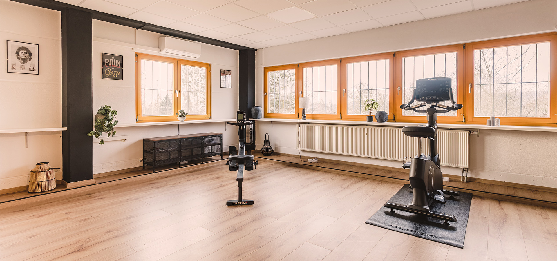 Modernes Fitnessraum der Physio Five Praxis in Merenberg mit zwei Fahrradergometern, viel natürlichem Licht durch große Fenster und sauberem Design für medizinisches Gesundheitstraining und Physiotherapie.