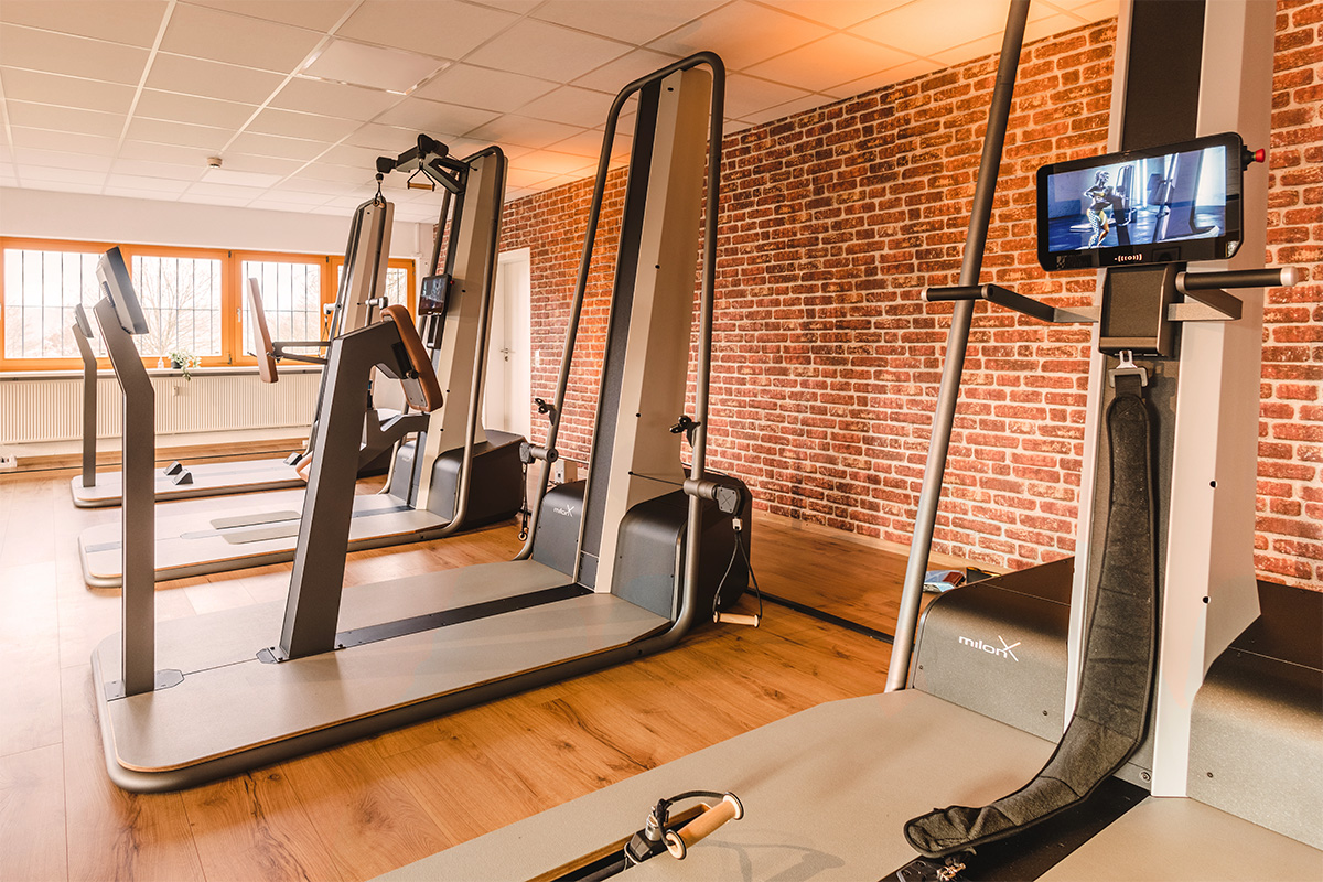 Modernes Gesundheitsstudio der Physio Five Praxis mit milon-Trainingsgeräten, Backsteinwand und hellem Holzfußboden – Raum für medizinisches Gesundheitstraining und Physiotherapie.
