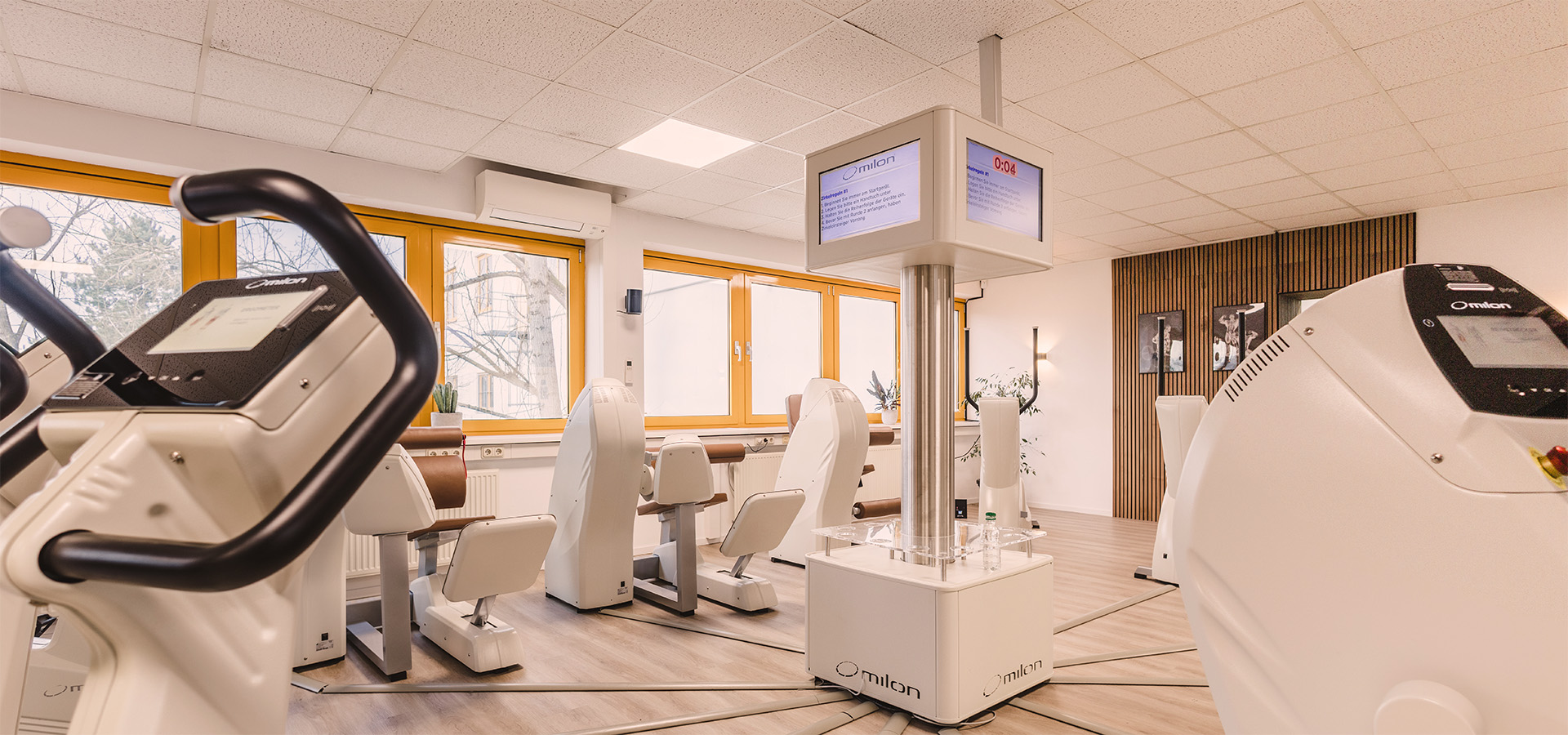 Helle, moderne Physiotherapiepraxis (Physio Five) mit milon-Trainingsgeräten und zentralem Display, ideal für die Kombination aus klassischer Physiotherapie und medizinischem Gesundheitstraining.